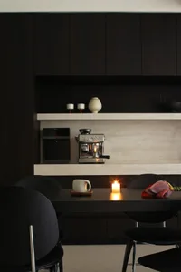 A sleek, minimalist black kitchen with a long table and chairs, decorated with a candle and plant.