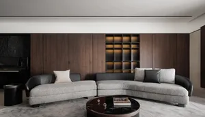 Modern living room with a curved gray sofa, white and black pillows, dark wood panels, and a round black coffee table on a li