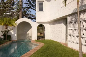 Modern architectural exterior featuring a white brick building with an arched entrance and a swimming pool in the foreground.