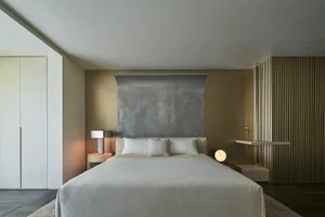 A minimalist bedroom featuring neutral-toned wall coverings and a large bed dressed in light-colored bedding.