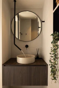 Modern minimalist bathroom featuring a wood vanity with a ceramic sink and black faucet, illuminated by a circular mirror.