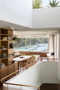 Modern minimalist living room with large windows overlooking a serene waterfront view, featuring wooden furniture and glass e