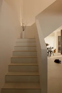 A modern, minimalist staircase with white concrete treads and modern railings, featuring a vase with dried branches on top of