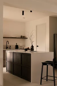 A minimalist black and white kitchen interior with a central island and bar stools.