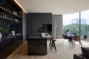 A modern kitchen and dining room featuring black marble countertops, black steel cabinets, and light wood flooring.