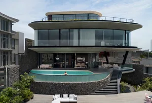 A modern house featuring a concrete exterior and glass elements with a person relaxing in the pool.
