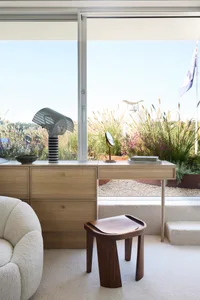 A modern residential space featuring wooden furniture, including a decorative lamp, a stool, and a desk with a mirror, all se