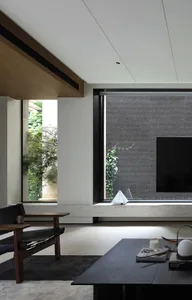Modern living room with wooden armchair, coffee table, and concrete floor, featuring a television and plants.