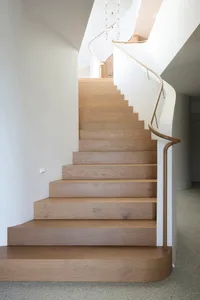 A modern wooden staircase with white walls and a curved handrail.