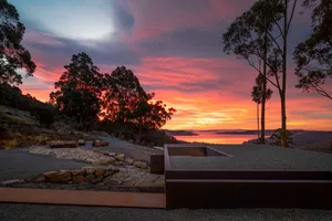 Concrete outdoor garden featuring a fire pit and wooden logs during a vibrant sunset.