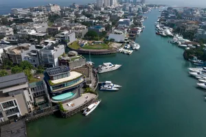 Aerial view of a waterfront development featuring concrete, glass, and timber structures with a pool and marina.