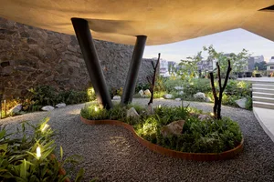 Industrial-style landscape design featuring concrete elements and stone planters under a modern, curved roof structure.