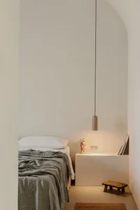 Minimalist bedroom with concrete walls, a wooden bench, and a concrete pendant light hanging above a bed.