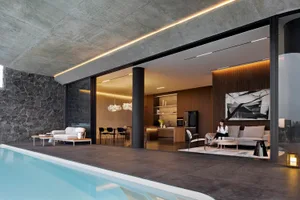 A modern living room with concrete walls and floor, featuring a sofa, coffee table, and illuminated ceiling lights.