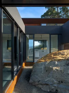 Modern house entry with glass cladding, featuring large glass doors and a stone rock.