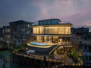 Modern luxury apartment with glass walls and concrete floors, featuring a swimming pool and outdoor seating area.