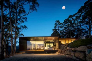 A modern house with a metal-clad exterior at dusk with a full moon in the sky.