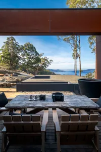 Modern, outdoor living space featuring concrete and wood furniture, surrounded by plants under a clear blue sky.