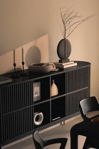 A modern sideboard made of black wood with geometric patterns, featuring decorative items such as a vase, candles, and books.