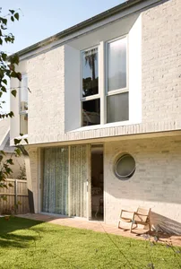 A modern residential exterior with white brick walls and large windows.