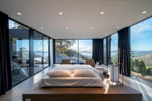 Modern bedroom featuring wood flooring, glass walls, and a view of the landscape.