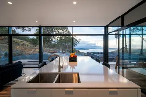 A modern kitchen featuring a large marble countertop with a stainless steel sink and a fruit bowl.
