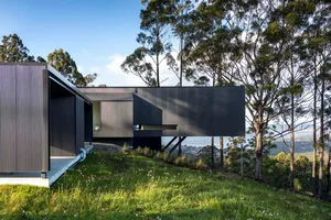 Modern exterior of a house with metal cladding, featuring a flat roof and large windows overlooking a scenic view.