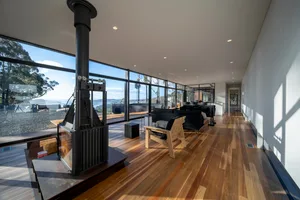 A modern living room with large windows, wooden floors, and black sofas.