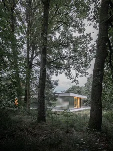 A minimalist house with glass walls nestled in a forested area.