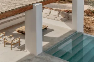Concrete poolside lounge seating with cushions under a wooden veranda.