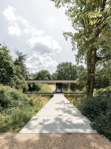 Modern house with glass walls and concrete pathway surrounded by greenery.