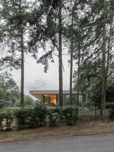 Modern house with glass and concrete exterior and interior lighting visible through large windows.