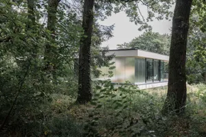 A modern residential house with a glass and steel exterior surrounded by trees.