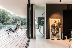 Modern minimalist living room with wooden flooring and furniture, featuring a large framed artwork on the wall.