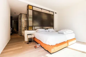 A minimalist bedroom featuring a wooden floor, white walls, and an orange bed frame.