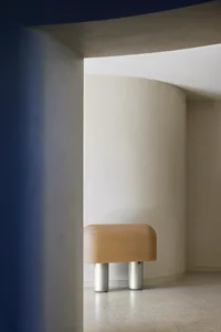A minimalist interior featuring a concrete and leather pouf in a curved, white space.