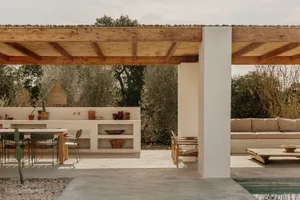 Outdoor living area with minimalist design, concrete floor and walls, wooden accents, and greenery in the background.