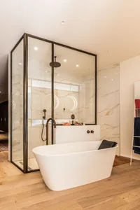 Modern bathroom with marble tiles, wood floor, and freestanding bathtub.