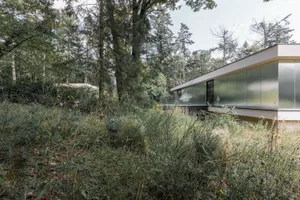 Modern house with metallic and glass exterior in a wooded area.