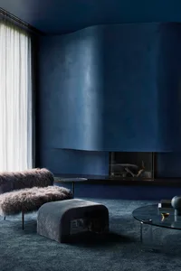 A modern industrial living room features plush, fur-covered seating and a sleek, glass-top coffee table with minimalist decor