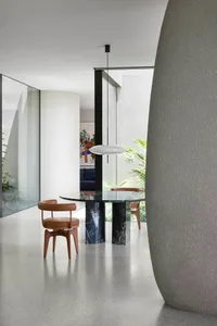 A modern minimalist dining area featuring a black marble table with concrete legs and a pendant light fixture.