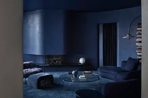 A modern minimalist living room with textured concrete walls and a dark blue color scheme, featuring a round glass coffee tab
