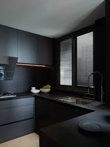 A modern, minimalist black kitchen with granite countertops, featuring a sink, stove, and minimalist design elements.