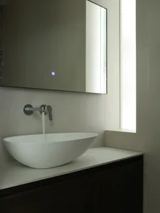 Modern minimalist bathroom with white ceramic sink and faucet, tall mirror, and frosted glass window.
