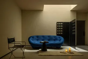 Modern blue sofa in a minimalist living room setting with a small table, candles, and a dark partition with circular designs.