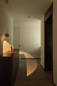 Modern corridor with concrete walls, wooden floors, and a hanging lamp casting light onto the floor.