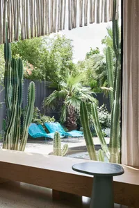 Modern living room featuring a concrete floor, blue lounge chairs, and a large window with a view of palm trees and swimming 