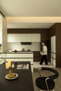 A modern kitchen featuring sleek wood cabinets and a marble countertop, with a woman walking past.