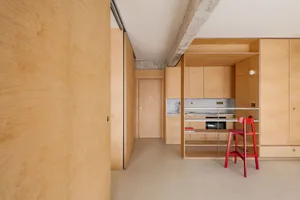 Modern kitchen with wooden cabinets and a red stool.