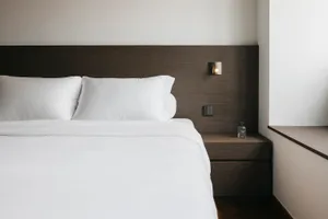 Modern minimalist bedroom featuring white bedding and dark wood headboard and nightstand
